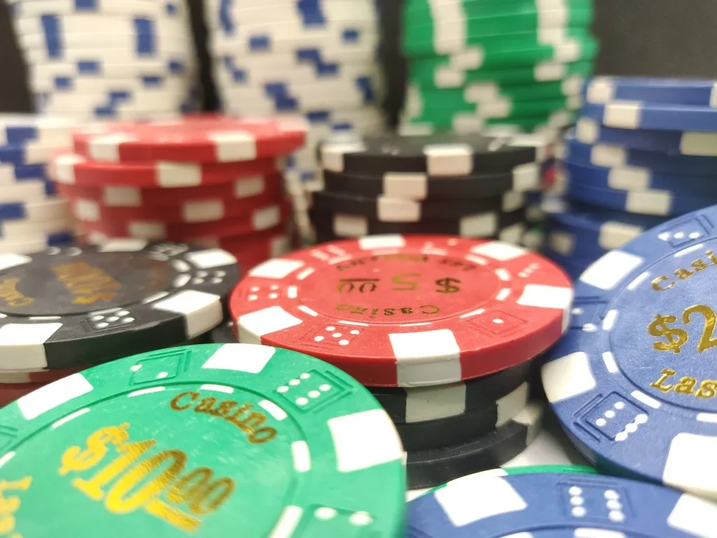 A close-up view of various stacks of colorful casino poker chips, including red, black, green, and blue, some with dollar values like $5, $10, and $25 visible.