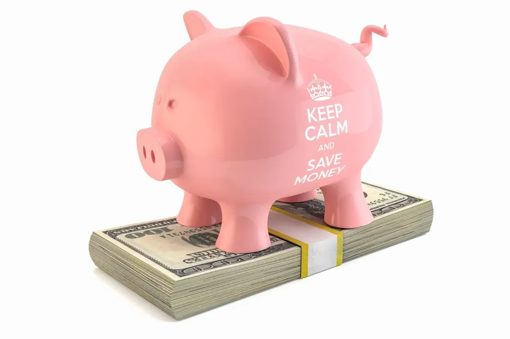A pink piggy bank with a crown logo and the text "KEEP CALM AND SAVE MONEY" printed on its side, standing on a thick stack of US hundred-dollar bills.
