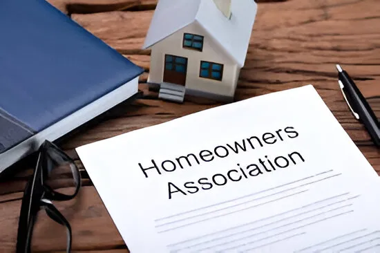 Document titled "Homeowners Association" on a wooden desk with a book, glasses, pen, and miniature house.