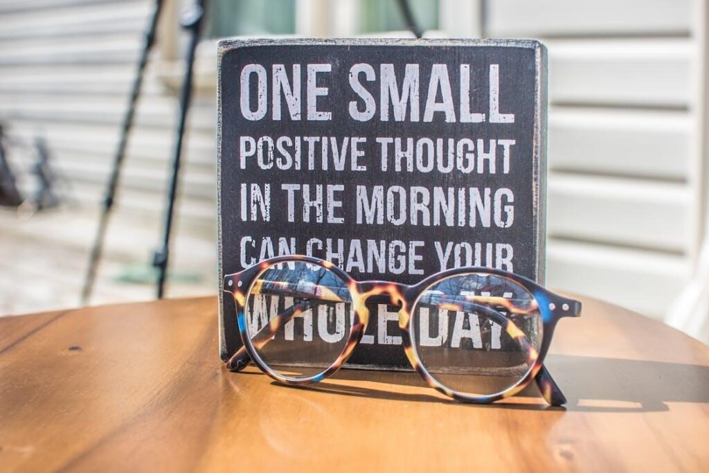 Reading glasses sit before a sign with an encouraging message about the power of positive thinking to transform the day.