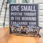 Reading glasses rest in front of a sign that reads "ONE SMALL POSITIVE THOUGHT IN THE MORNING CAN CHANGE YOUR WHOLE DAY."