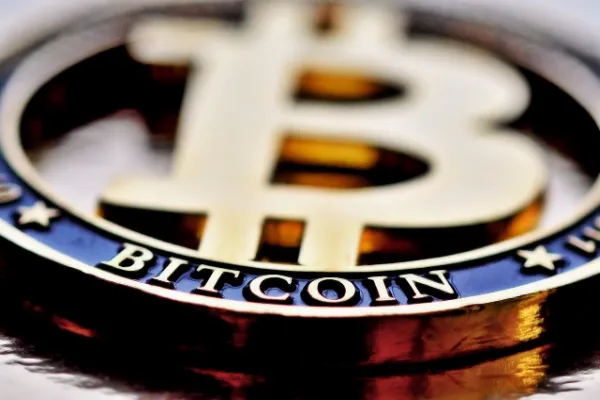 Gold-colored Bitcoin logo with "BITCOIN" clearly visible on the lower blue band, representing digital currency and modern finance.