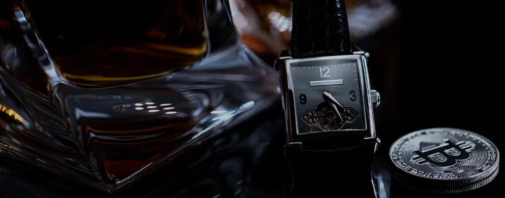 A luxurious scene featuring a square-faced Girard-Perregaux vintage watch with an exposed tourbillon, a glass of amber liquid (likely whiskey or cognac), and a silver Bitcoin coin, all set against a dark, reflective background.