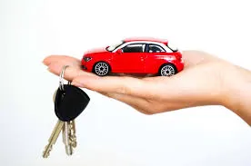 Hand holding a toy red car and car keys, representing new car ownership and auto loan considerations.