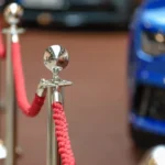 Red velvet ropes and polished stanchions at a glamorous event entrance with luxury cars in the background
