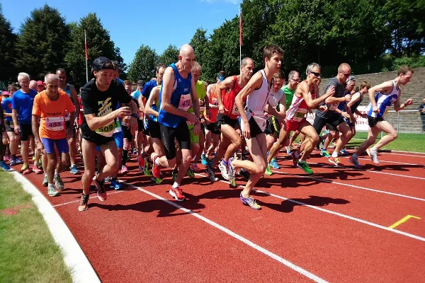 A group of runners of varying ages and abilities are captured in motion at the start of a race on a red track under a sunny sky, embodying the effort of a personal journey.