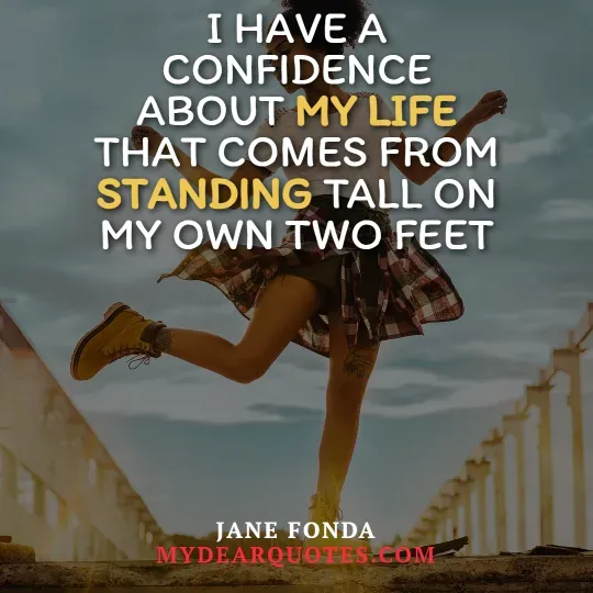 A woman in a plaid shirt tied around her waist, shorts, and yellow work boots is shown mid-step, balancing on what appears to be a concrete ledge or wall, with a clear sky in the background. She has a visible tattoo on her leg. Overlaying the image is the quote "I HAVE A CONFIDENCE ABOUT MY LIFE THAT COMES FROM STANDING TALL ON MY OWN TWO FEET." The words "MY LIFE" and "STANDING" are highlighted in yellow. The quote is attributed to Jane Fonda, with "MYDEARQUOTES.COM" visible below.