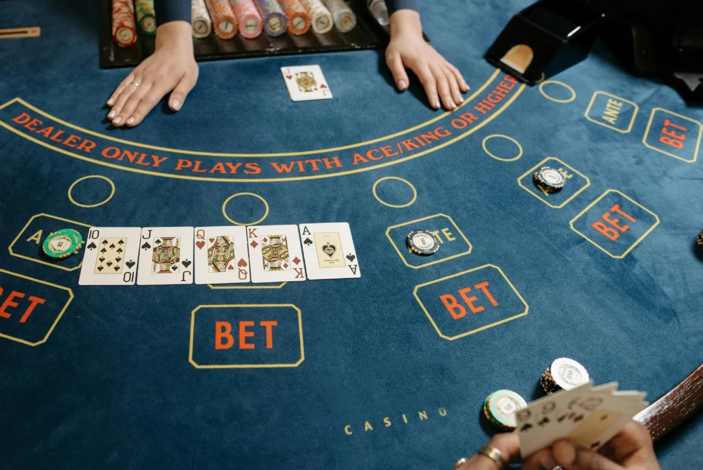 Top-down view of a casino Baccarat table with hands, cards like Ace and King, and stacks of colorful poker chips, signifying a high-stakes card game.