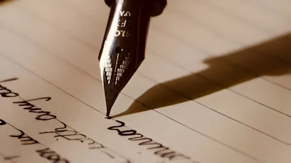 A close-up of a fountain pen nib writing on lined paper, with handwritten cursive text visible.