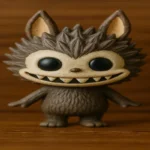 A mischievous-looking, light brown monster toy with large, pointed ears, big eyes, and a wide, impish smile, standing with its arms slightly out to the sides.