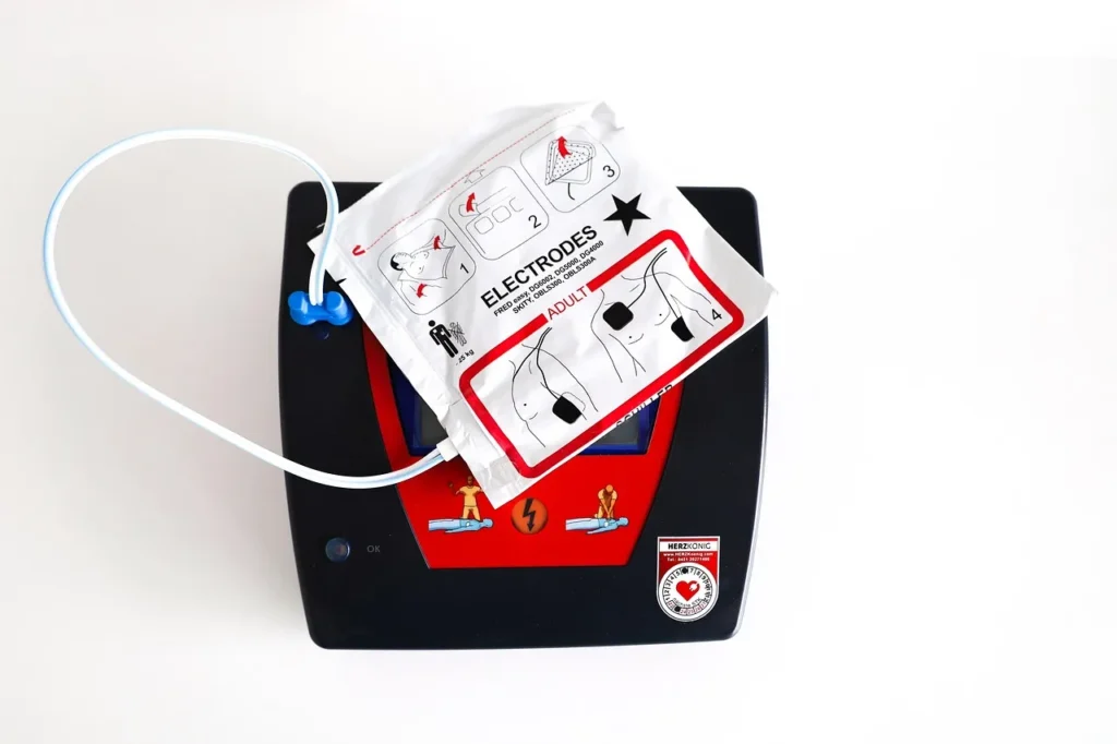 A top-down view of a black AED (Automated External Defibrillator) with a package of adult electrode pads resting on top.