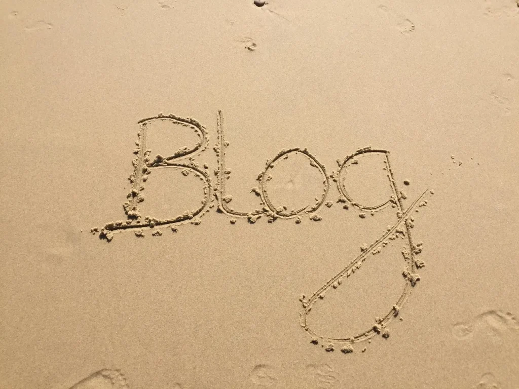 The word "Blog" written in the sand on a beach.