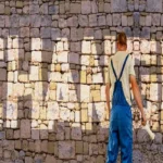 A person in overalls facing a stone wall with the word "CHANCE" illuminated on it.