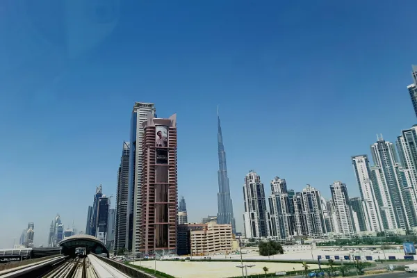 A wide view of the Dubai skyline under a clear blue sky, featuring numerous modern high-rise buildings and a metro line in the foreground, not specifically focused on JBR.