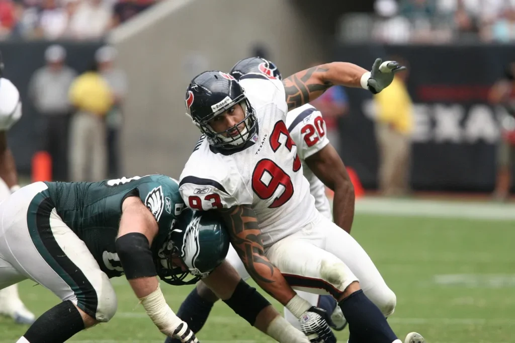 Two American football players in white and green jerseys aggressively tackling each other on a green field during a professional NFL game, symbolizing the action and intensity of the football season.