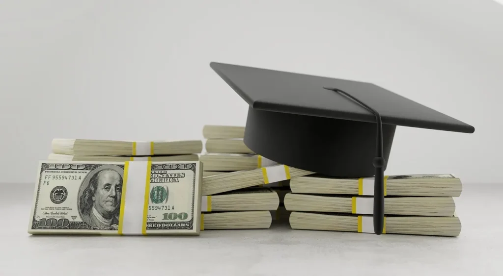 A black graduation cap with a tassel sitting on top of several large stacks of bundled US hundred-dollar bills.