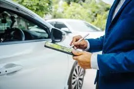 An insurance adjuster or lawyer in a suit using a digital tablet to document a car at the scene of an accident.