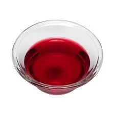 A small, clear glass bowl containing a vibrant, transparent red liquid, likely a natural food coloring extract.