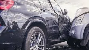 Close-up of a severe side-impact car accident showing extensive damage to the door and fender of a dark-colored SUV, with another vehicle's front end impacting it.