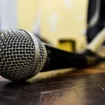 A close-up of a professional-grade microphone lying on a dark wooden surface, symbolizing the act of speaking, explaining, or broadcasting a viral trend.
