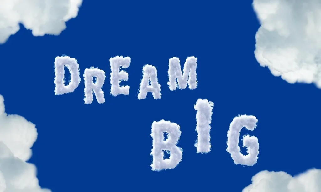 The words "DREAM BIG" formed by fluffy white clouds against a vibrant blue sky, with other clouds framing the edges.