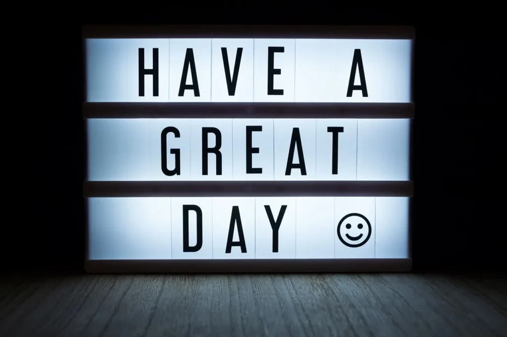 A glowing white lightbox sign displaying the black text "HAVE A GREAT DAY" with a smiley face icon, set against a dark background.