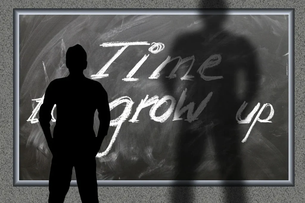 A silhouette of a person standing in front of a chalkboard with the phrase "Time to grow up" written in chalk, with the person's shadow overlapping the text.