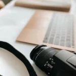 An overhead close-up of a person's hands using a laptop on a wooden table, with their credit card placed next to the keyboard, symbolizing earning a living from a digital side hustle or online business.