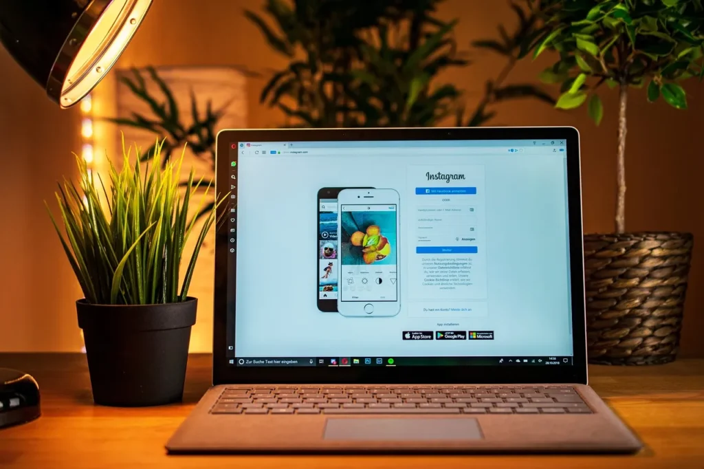 A laptop screen displaying the Instagram login and registration page, set on a desk next to a potted plant, representing the digital platform central to influencer marketing.