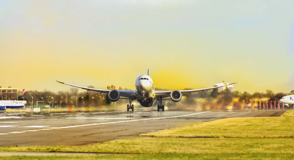 Front view of a large commercial airplane taking off from a wet runway at sunset, symbolizing affordable global travel and expert flight booking.